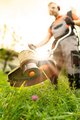 Close up of man using grass trimmer for cutting lawn in his garden on sunny summer day.