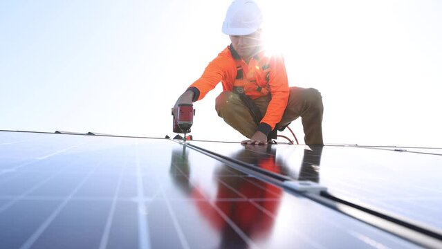 Solar panel technician with drill installing solar panels on house roof on a sunny day.