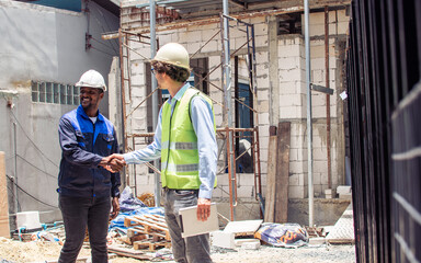 Two diversity male engineers team working, inspecting outdoor at construction site, wearing hard hats for safety, talking, discussing. Career, Industry Concept.