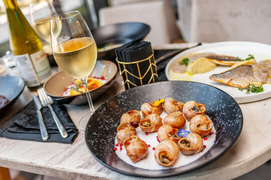 Cooked grape snails in shells on a table in a restaurant with a glass of white wine