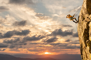 Woman climbing at sunset on mountain golden colors, feeling security and confidence - obrazy, fototapety, plakaty