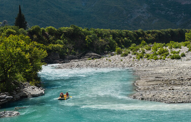 White water rafting. Adventure and sport. A yellow raft floating among the rocks on the crystal clear, blue-green water. Perpendicular drone view of the rafters floating on Vjose river, Albania. 