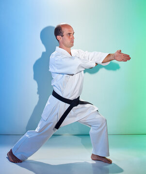 Adult man with black belt training formal exercises against color background with blue and green tint