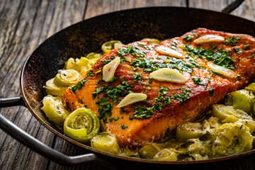 Fried salmon steak with cooked leek and garlic on frying pan on wooden table