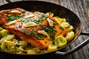 Fried salmon steak with cooked leek and garlic on frying pan on wooden table