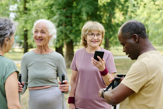 Group Of Senior People Meeting Outdoors To Train, They Talking To Each Other And Using Smartphone