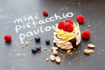 Close up of mini pistachio pavlova cake with fresh raspberries and blueberries on black chalk board