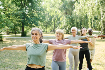 Senior people standing in a row and doing exercises together with coach outdoors