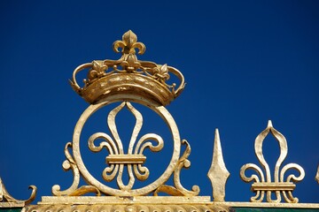 Gold Crown And Fleur-De-Lis On The Grand Trianon Gates Against A Blue Sky In The Gardens Of The...