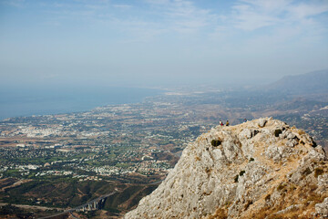 Two Mountain Climbers Sitting On A Peak Overlooking The City; Marbella, Malaga, Andalusia, Spain
