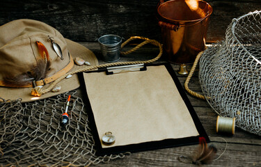 Clipboard with vintage paper for your text logo or info. Fishing tackles, cap, net, bucket on a...