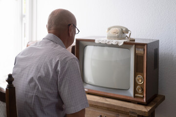elderly man turns on and watches old retro analog TV with blank screen for designer, white background, 1960-1970, stylish mockup, template for video, Retro Technology in Everyday Life