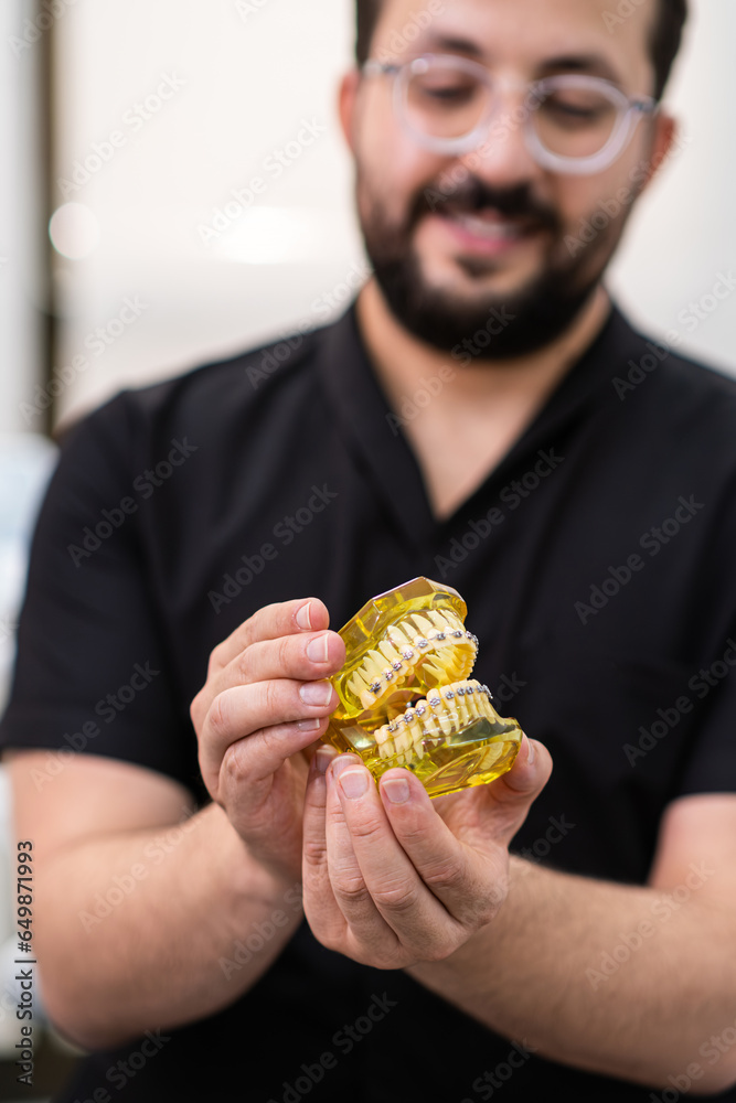 Aufkleber smiling dentist in black uniform showing open artificial human jaws with installed dental braces for