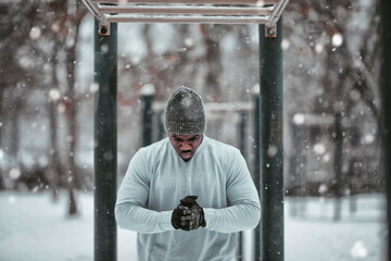 Young African American man getting ready to do exercises on the monkey bars in an outdoor park during winter and snow