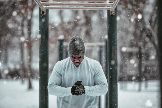 Young African American man getting ready to do exercises on the monkey bars in an outdoor park during winter and snow