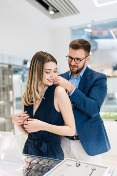 Beautiful couple enjoying in shopping at modern jewelry store. Young woman try it out gorgeous necklace and earrings. Fashion style and elegance concept.