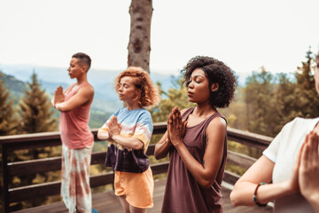 Young and diverse group of female friends doing yoga on a balcony of a cabin house in nature