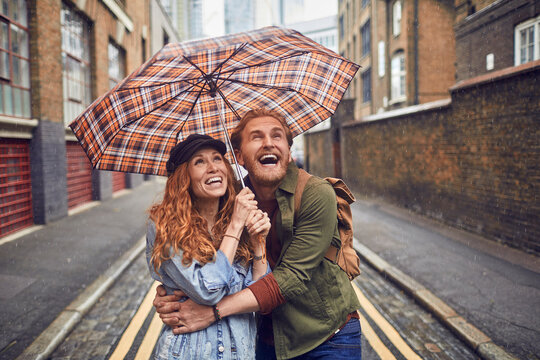 Young redhead couple using a umbrella to avoid the rain while on a date in London UK