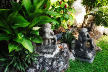A garden with a stone statue and various plants. It statue  made of stone and appears weathered....