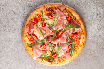 Pizza with prosciutto, ham, arugula, tomatoes, pesto, cheese and parmesan. Italian cuisine. 