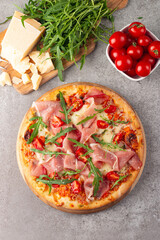 Pizza with prosciutto, ham, arugula, tomatoes, pesto, cheese and parmesan. Italian cuisine. 
