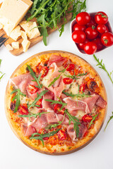 Pizza with prosciutto, ham, arugula, tomatoes, pesto, cheese and parmesan. Italian cuisine. 