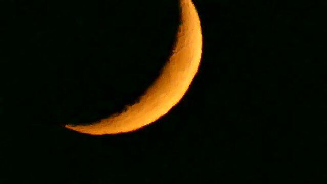 Dark night sky and orange and yellow crescent moon with visible fragments of craters - natural view before moonset in real time. Topics: astronomy, optical phenomenon, atmosphere, cosmos, science