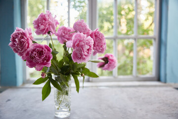 Peonies in a vase on the table against the background of the window.