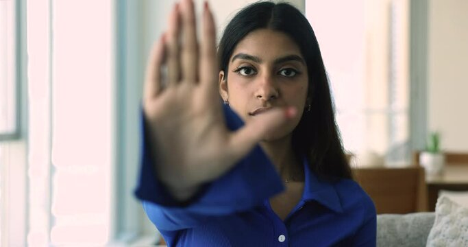 Close up young serious Indian female stretch out her palm to camera, makes stop gesture, struggle for women rights, against abuse or bullying, express opinion about abortion and racial discrimination