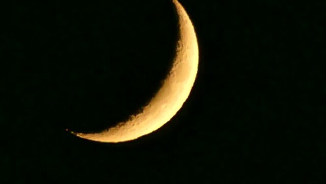 Dark night sky and orange and yellow crescent moon with visible fragments of craters - natural view before moonset in real time. Topics: astronomy, optical phenomenon, atmosphere, cosmos, science