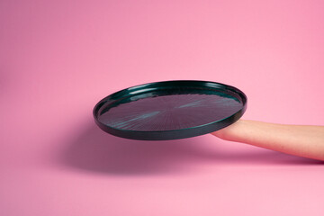 Empty green plate held in hand. Pink background.