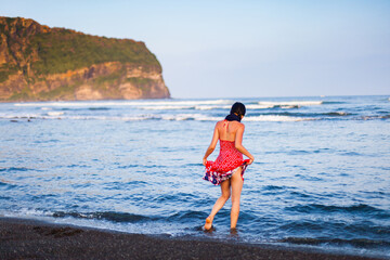Young Korean Woman on a black sand beach, watches the sea, ilchungbong in the background, Seongsan, Jejudo, South Korea
