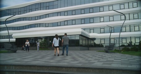 Courtyard of modern medical facility. Medical staff and diverse people enter and exit the hospital. Woman with physical disability rides to clinic on motorized wheelchair on appointment with doctor.