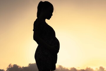 A pregnant woman holding her belly walking outdoor, sunset silhouette.