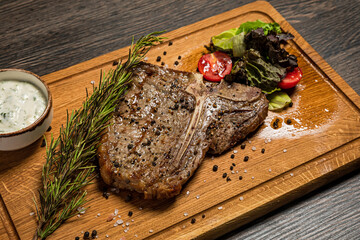 T-bone steak served on a wooden board with sauce, fresh vegetables and rosemary