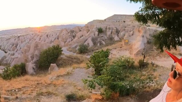 A tourist girl admiring the sunset view on Red Valley Park in the heart of Cappadocia of Turkey, as the sun sets, casting a romantic and golden hue over the surreal landscape.
