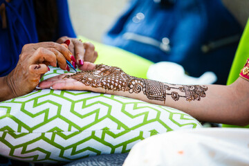 Closeup of henna tattoos being applied to a person in traditional Indian attire at a wedding.