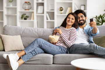 Happy young indian couple watching TV together at home