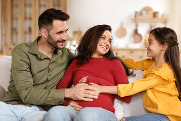 Girl Touching Mom's Pregnant Belly Sitting With Dad At Home