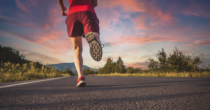 Fitness blonde woman running on the asphalt road at the mountains