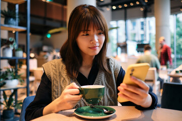 Asian young woman using her cell phone having a coffee
