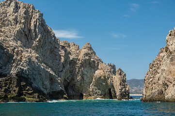 Fototapeta na wymiar Mexico, Cabo San Lucas - July 16, 2023: South view on Reserva de Los Marina, open channel between tall gray boulders in greenish ocean water. Cityscape and beach on horizon
