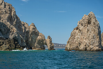 Fototapeta na wymiar Mexico, Cabo San Lucas - July 16, 2023: South view on Reserva de Los Marina, El Arco and channel between tall gray boulders in greenish ocean water. Cityscape and beach on horizon