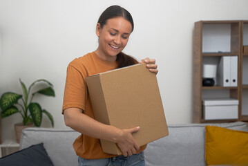 Smiling woman examines cardboard box with ordered goods in apartment room female happy with order...