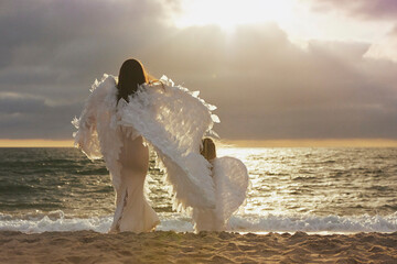 Mom and daughter dressed as angels on the sea at sunset