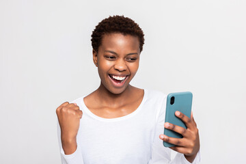 Happy winner african teenager woman using smart phone isolated over white background raising fist up celebrating winning lottery victory concept fortunate woman