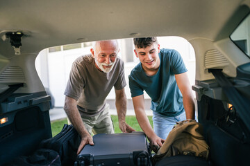 Two men Teenager and senior grandfather pack baggage in trunk of car