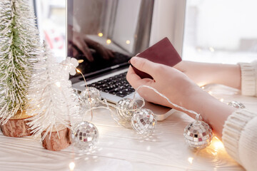 Planning Christmas. Buying invitations and decorations online. Hand holding a bank card against the background of a laptop