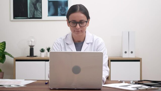 Young female doctor reviews examination of patient organs on laptop medical specialist works sitting at table with pictures and documents in modern clinic