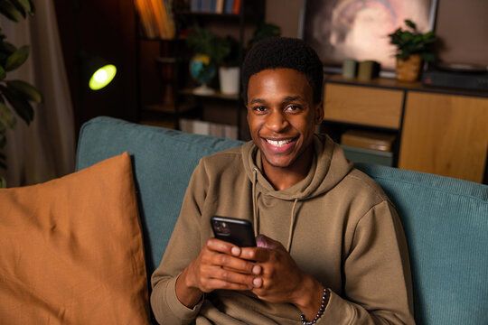 Happy delighted African American dark skinned young man checking his social media notifications on his phone, feeling connected to the world and his online community